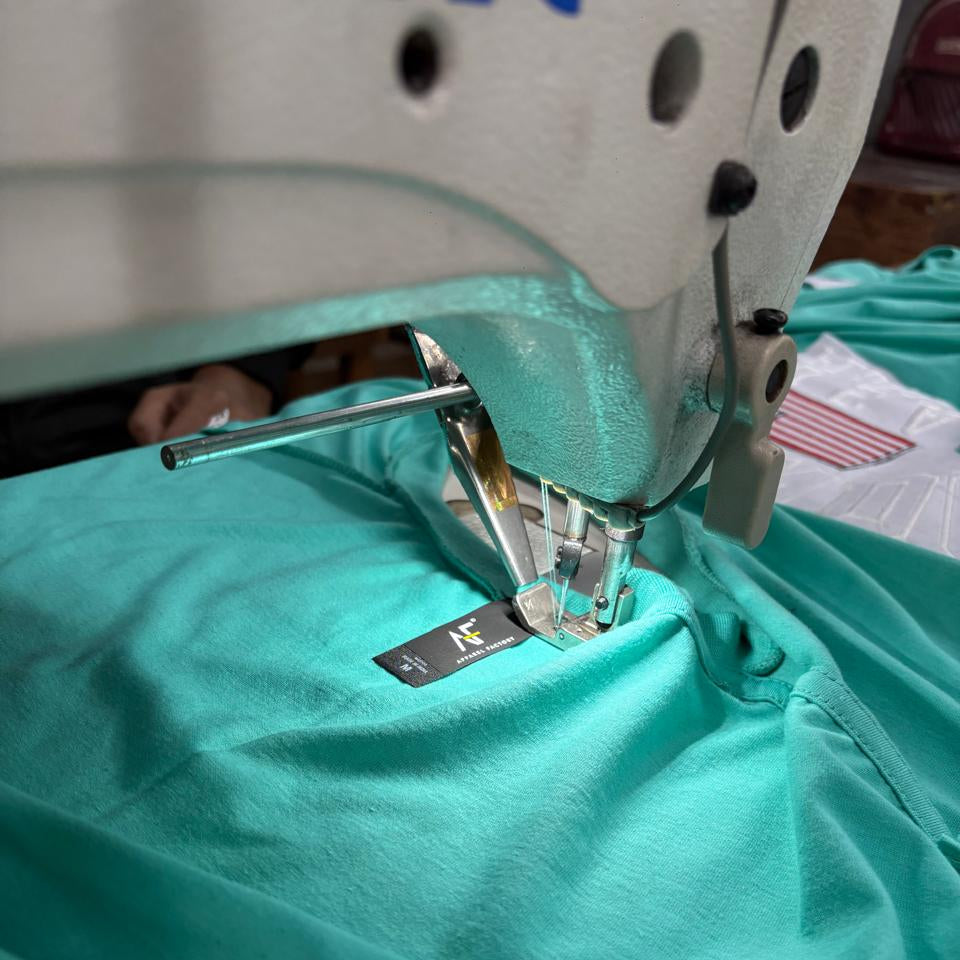 Stitching of Apparel Factory label to AF810 mint tee in manufacturing facility.
